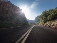 the long road passes through some very steeply rocky mountains under a beautiful sun and blue sky