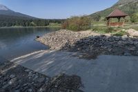 a bench on a rocky shore next to a lake and mountains in the background,