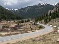 a mountain side with a road running next to the mountains, a bike parked in front of it and trees on one side