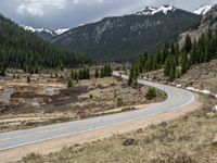 a mountain side with a road running next to the mountains, a bike parked in front of it and trees on one side