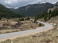 a mountain side with a road running next to the mountains, a bike parked in front of it and trees on one side