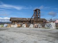 there is a old abandoned mine building by rocks with graffiti all over it and mountains behind