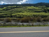 the road is paved with yellow markings and has a snowy mountain range in the background