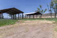 a dirt road with a covered pavilion in the distance at a farm near a green grassy field