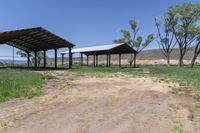 a dirt road with a covered pavilion in the distance at a farm near a green grassy field