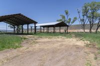 a dirt road with a covered pavilion in the distance at a farm near a green grassy field