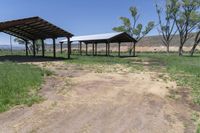 a dirt road with a covered pavilion in the distance at a farm near a green grassy field