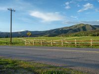 a lone country road is in the countryside area with mountains on both sides and barbed fence between the two sides