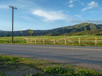 a lone country road is in the countryside area with mountains on both sides and barbed fence between the two sides