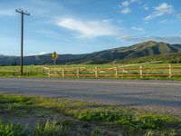 a lone country road is in the countryside area with mountains on both sides and barbed fence between the two sides