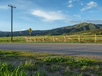 a lone country road is in the countryside area with mountains on both sides and barbed fence between the two sides