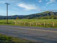 a lone country road is in the countryside area with mountains on both sides and barbed fence between the two sides