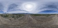 a large lens is reflected in the view of a desert dirt road with a couple of small clouds in the sky