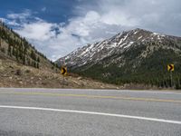 a mountain side with a road running next to the mountains, a bike parked in front of it and trees on one side