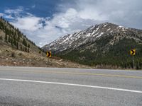 a mountain side with a road running next to the mountains, a bike parked in front of it and trees on one side