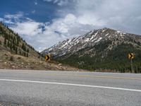 a mountain side with a road running next to the mountains, a bike parked in front of it and trees on one side