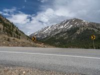 a mountain side with a road running next to the mountains, a bike parked in front of it and trees on one side