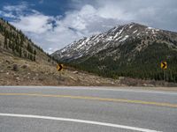 a mountain side with a road running next to the mountains, a bike parked in front of it and trees on one side