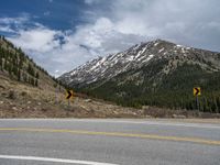 a mountain side with a road running next to the mountains, a bike parked in front of it and trees on one side