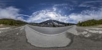 a panoramic photo of an empty road at the bottom of mountains, with a mountain in the background