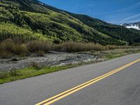 the road is paved with yellow markings and has a snowy mountain range in the background