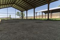 the inside of an empty barn with hay around and on the floor is a big open air shelter