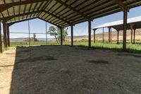 the inside of an empty barn with hay around and on the floor is a big open air shelter