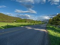 a empty road that goes through a grassy area with mountains in the background as well as trees