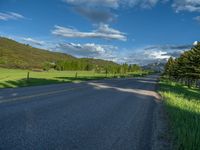 a empty road that goes through a grassy area with mountains in the background as well as trees