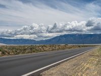 an empty empty road with mountain in the background in the desert, looking at some clouds above