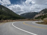 a mountain side with a road running next to the mountains, a bike parked in front of it and trees on one side