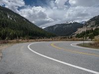 a mountain side with a road running next to the mountains, a bike parked in front of it and trees on one side