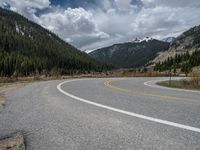 a mountain side with a road running next to the mountains, a bike parked in front of it and trees on one side