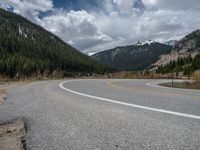 a mountain side with a road running next to the mountains, a bike parked in front of it and trees on one side