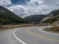 a mountain side with a road running next to the mountains, a bike parked in front of it and trees on one side