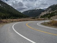 a mountain side with a road running next to the mountains, a bike parked in front of it and trees on one side