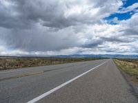 a road with an asphalt roadhead next to grass and dirt, under a cloudy sky