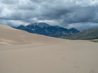 someone is going through the sand dunes with mountains in the background during daytime on a cloudy day