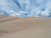 a desert with sand and clouds in the background and person on horseback in the distance