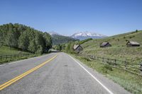 a scenic road runs through a valley with mountains behind it, and a wooden fence, along the far end of the street