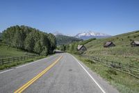 a scenic road runs through a valley with mountains behind it, and a wooden fence, along the far end of the street