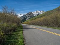 the road is paved with yellow markings and has a snowy mountain range in the background