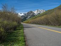 the road is paved with yellow markings and has a snowy mountain range in the background