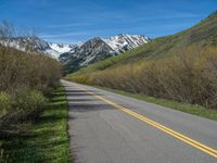 the road is paved with yellow markings and has a snowy mountain range in the background