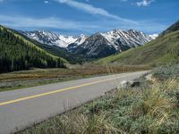 the road is paved with yellow markings and has a snowy mountain range in the background