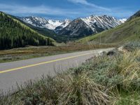 the road is paved with yellow markings and has a snowy mountain range in the background