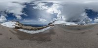 a panorama lens is over an icy, snowy ground and mountains under a cloudy sky