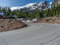 the curved road is near an evergreen mountain side area with rocks and trees in winter