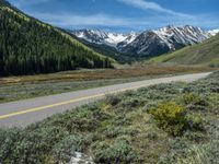 the road is paved with yellow markings and has a snowy mountain range in the background