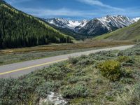 the road is paved with yellow markings and has a snowy mountain range in the background